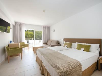 Helles Hotelzimmer mit Doppelbett, Sofa, Sesseln und Balkon mit Blick ins Grüne.
