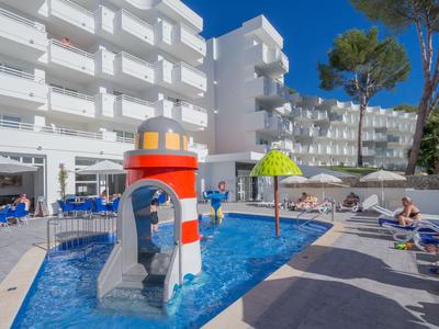 Hotelpool mit Kinderwasserspielplatz und mehreren Etagenwohnungen im Hintergrund.