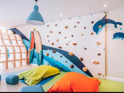 Heller Spielraum mit Kletterwand, blauen und orangen Sitzsäcken, Holzrutsche und Delfinwanddeko.