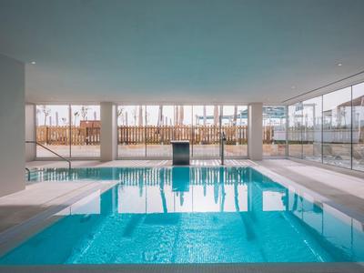 Innenraum mit großem, rechteckigem Hallenbad und großen Fenstern an einer Seite.