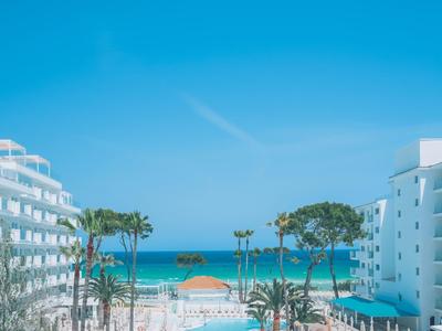 Blick auf blauen Himmel, Meer, Hotels und Palmen zwischen weißen Gebäuden bei sonnigem Wetter.