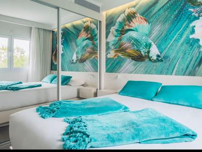 Kleines Schlafzimmer mit weißem Bett, türkisblauer Decke und Kissen, großer Wolf-Wandkunst.