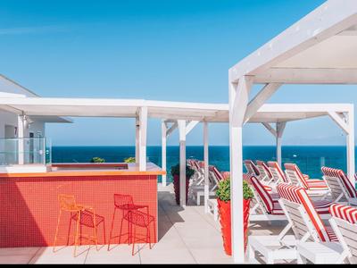 Moderner Dachpool mit roten Liegestühlen und Bar, blauer Himmel und Meerblick im Hintergrund.