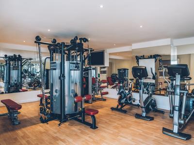 Hell eingerichteter Fitnessraum mit modernen Geräten, Fahrrädern und Spiegelwänden.