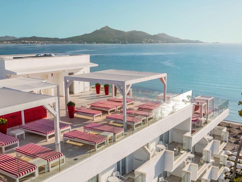 Hotelterras met rode ligstoelen en zeezicht bij heldere lucht.