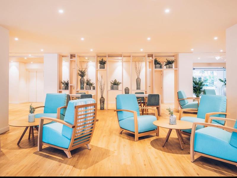 Lichte lounge met comfortabele blauwe fauteuils en houten vloeren in een modern hotel.