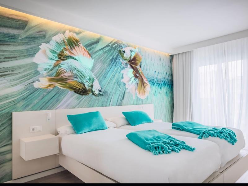 Moderne hotelkamer met tweepersoonsbed, turquoise accenten en vissenwanddecoratie.