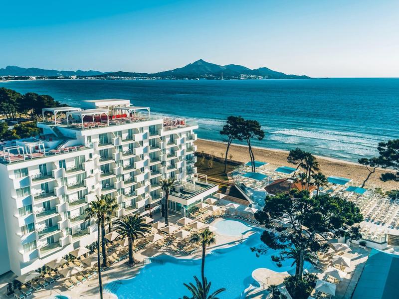 Modern hotel met zwembad, palmbomen en uitzicht op zandstrand en zee.