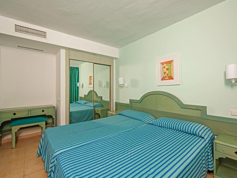 Ein schlicht eingerichtetes Schlafzimmer mit blau gestreiftem Bett und Spiegel-Kleiderschrank.