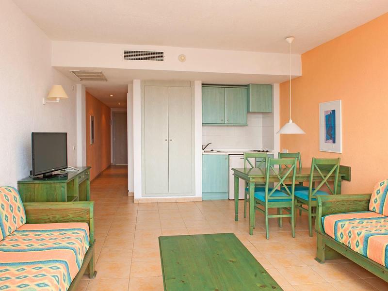 Helles Wohnzimmer mit orangefarbener Wand, grünen Möbeln und offener Küchenecke.