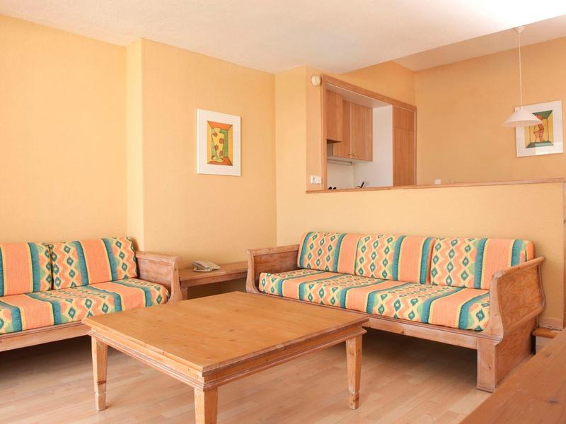 Hell eingerichtetes Wohnzimmer mit zwei gemusterten Sofas, Holztischen und pastellfarbenen Wänden.