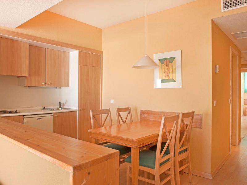 Heller Essbereich mit Holztisch und Stühlen, daneben kleine Küche mit Holzschränken.