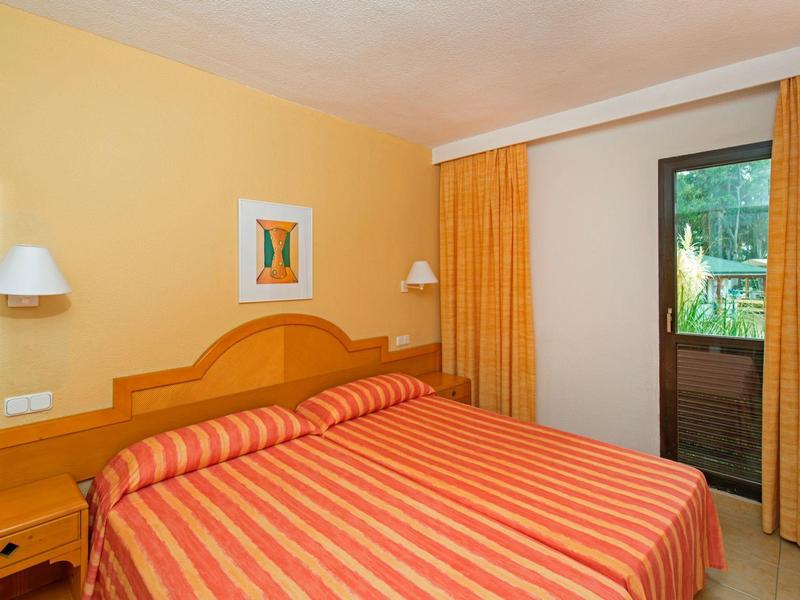 Schlafzimmer mit Doppelbett, orangem Streifenbettwäsche, Holzmöbeln und gelben Vorhängen.