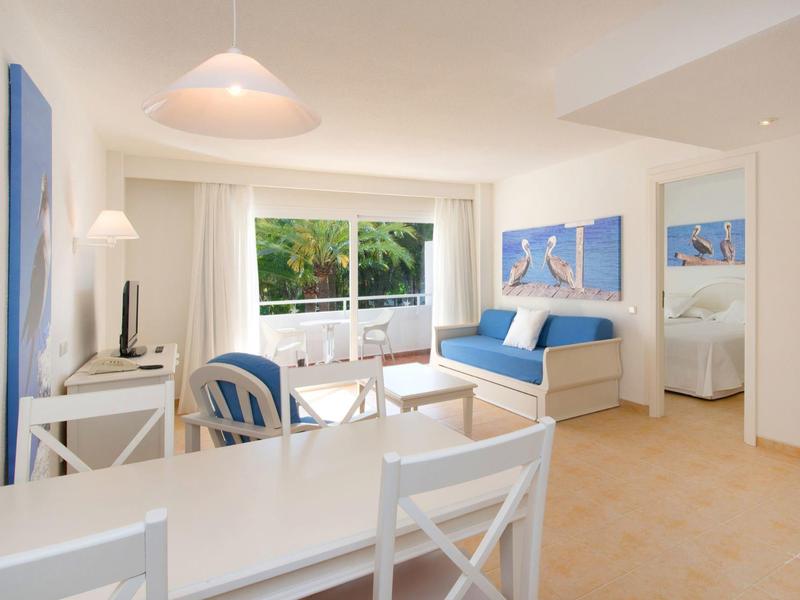 Heller Wohnzimmerbereich mit weißen Möbeln, blau-weißen Kissen und großen Fenstern zum Garten.