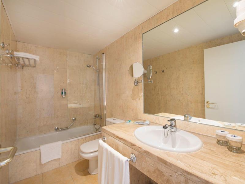 Helles Badezimmer mit beiger Marmoroptik, Badewanne, Waschbecken und großem Spiegel.