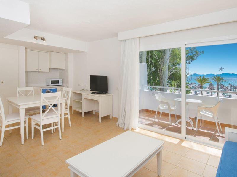 Helles Wohn- und Esszimmer mit weißem Mobiliar und großem Fenster zur Terrasse mit Meerblick.