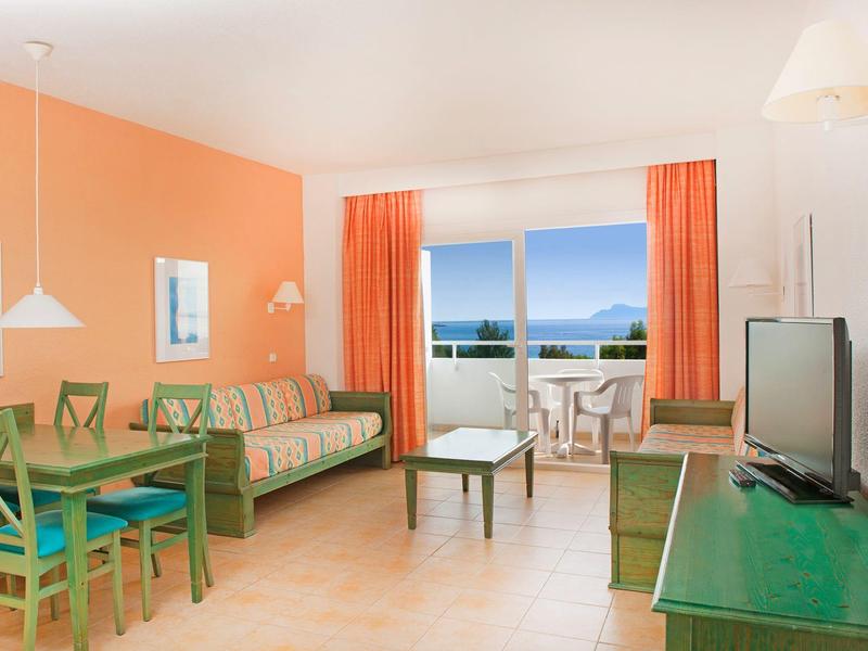 Großes Wohnzimmer mit orangener Wand, grünen Möbeln und Balkon mit Meerblick.