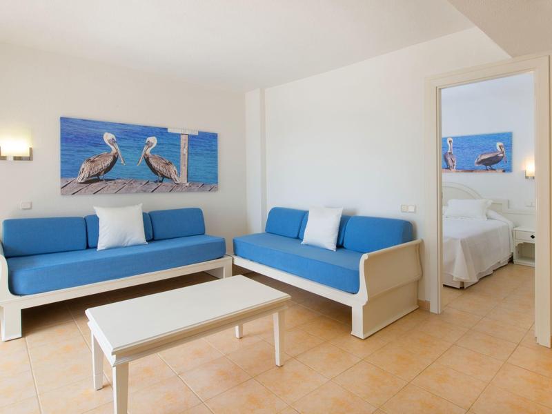 Helles Wohnzimmer mit blauen Sofas, weißem Tisch und Wandbildern von Pelikanen über dem Sofa.