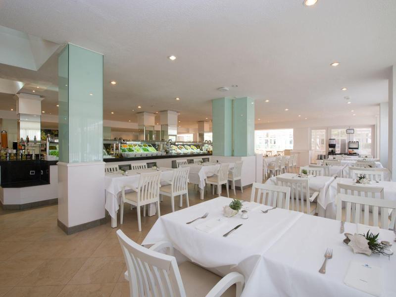 Ein heller, moderner Gastraum mit weißen Tischen, Stühlen und minimalistischer Dekoration.