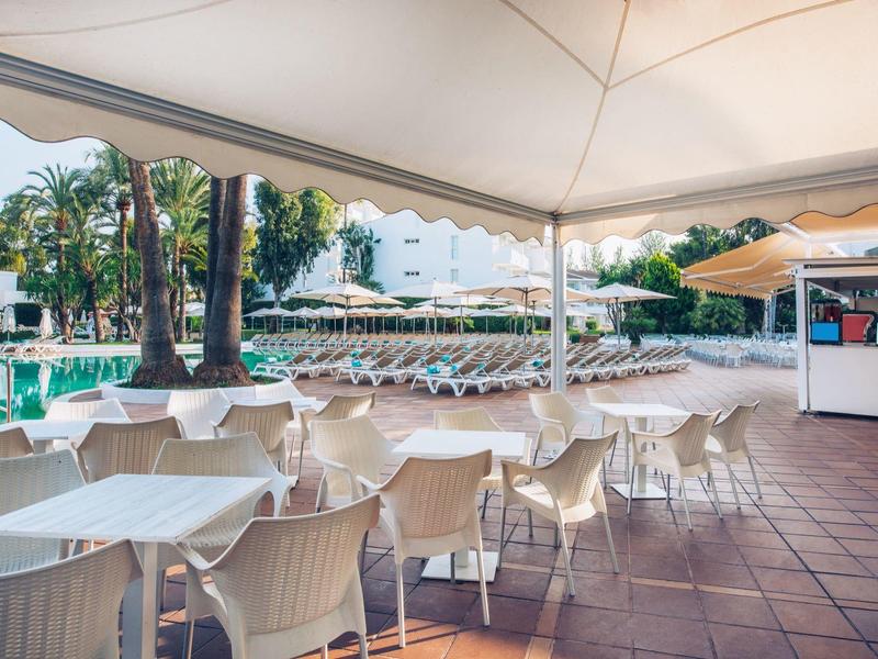 Leerer Außenbereich mit weißen Tischen und Stühlen unter Sonnenschirmen neben einem Pool.
