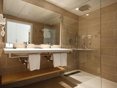 Modernes Badezimmer mit großem Spiegel, weißem Waschbecken und braunen Fliesen an Wand und Boden.