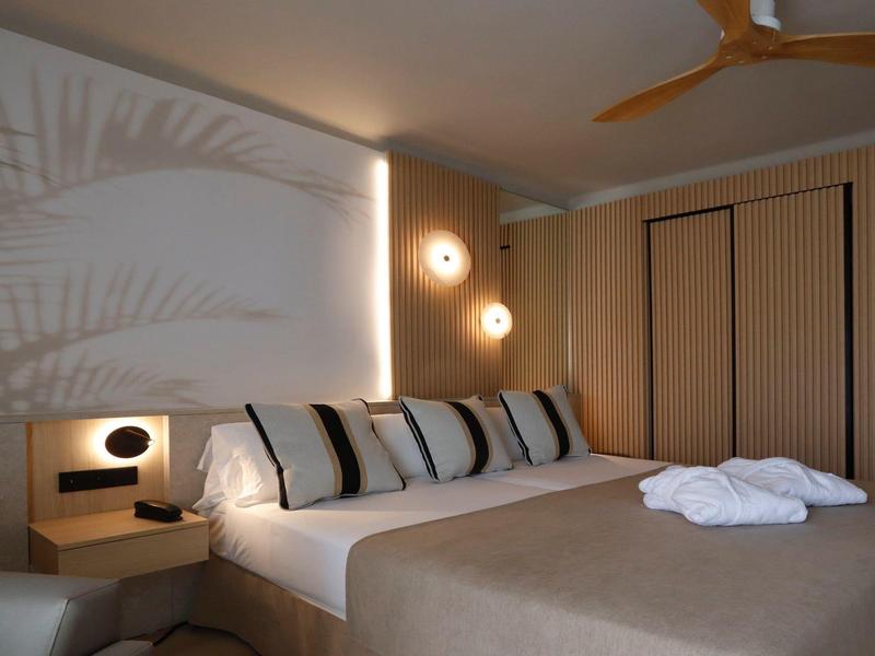 Habitación de hotel moderna con cama doble, paredes claras, ventilador de techo y iluminación elegante.