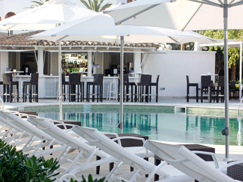 Área de piscina con tumbonas blancas y sombrillas junto a modernos grupos de asientos.