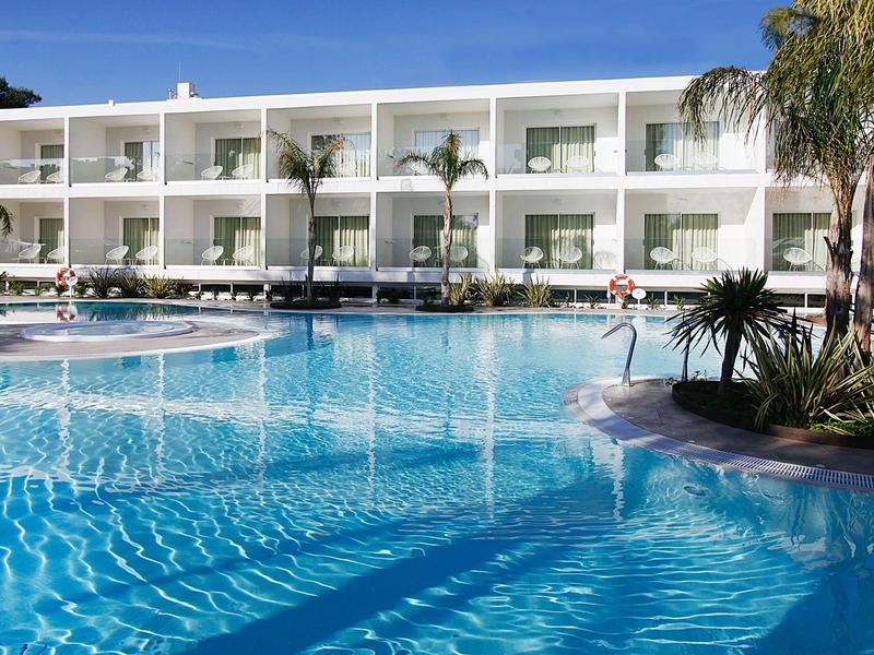 Gran hotel con piscina azul y palmeras bajo cielo despejado.