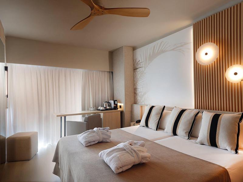 Habitación de hotel moderna con cama grande, varias almohadas y luz natural desde la terraza.