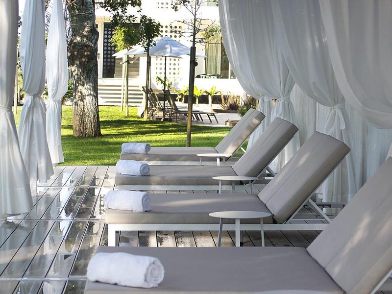 Cómodas tumbonas con toallas blancas bajo cortinas transparentes blancas en un jardín.