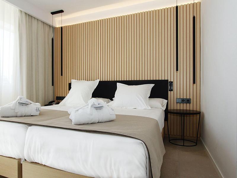 Habitación de hotel moderna con cama doble, colcha beige y varillas decorativas en la pared.