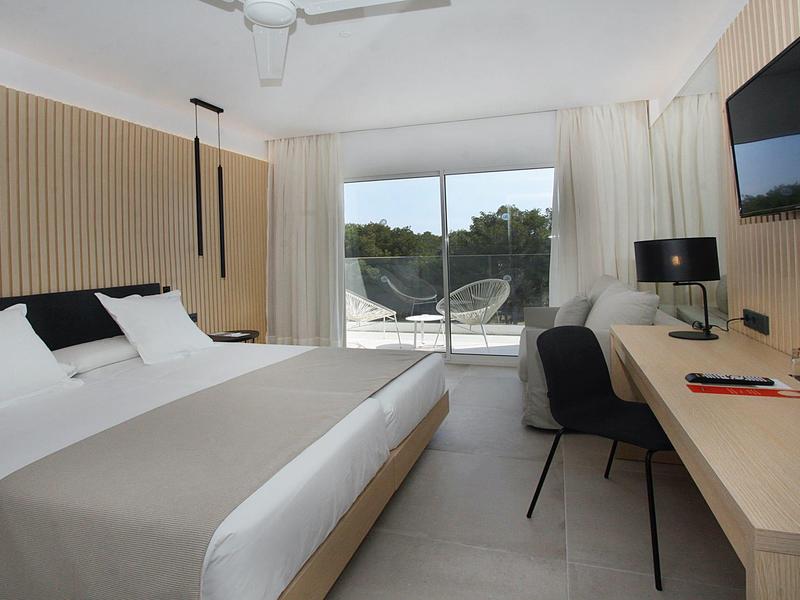 Habitación con cama doble, escritorio, silla, gran ventanal y cortinas en diseño claro.