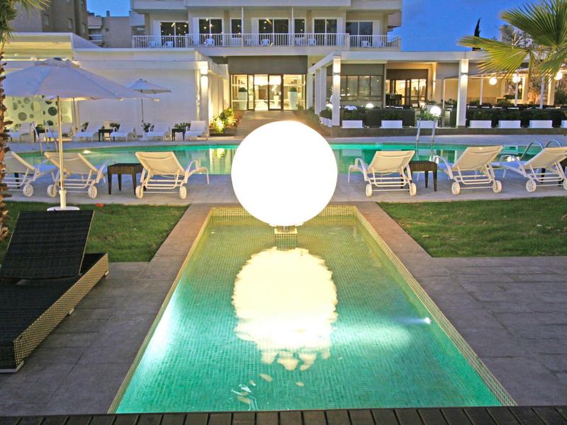 Piscina iluminada con áreas de descanso y palmeras en hotel moderno por la noche.