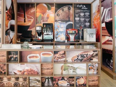 Nowoczesny bar kawowy z ekspresem do kawy i muralem ściennym prezentującym różne specjały kawowe