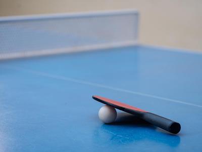 Rakietka i piłka do tenisa stołowego leżą na niebieskim stole do ping-ponga.