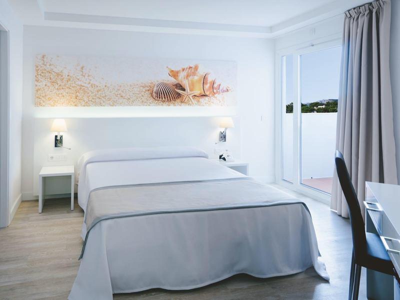 Nowoczesny pokój hotelowy z podwójnym łóżkiem, biurkiem i balkonem z widokiem na zieleń.