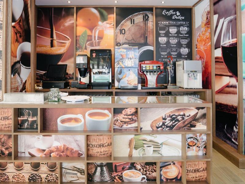 Nowoczesny bar kawowy z ekspresem do kawy i muralem ściennym prezentującym różne specjały kawowe