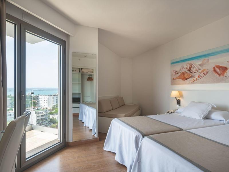 Jasny pokój hotelowy z dwoma pojedynczymi łóżkami, balkonem i widokiem na morze.