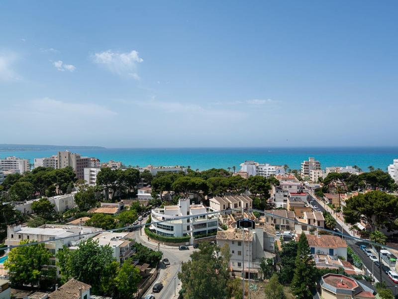 Widok na nadmorskie miasto z nowoczesnymi budynkami, drzewami i morzem w tle.