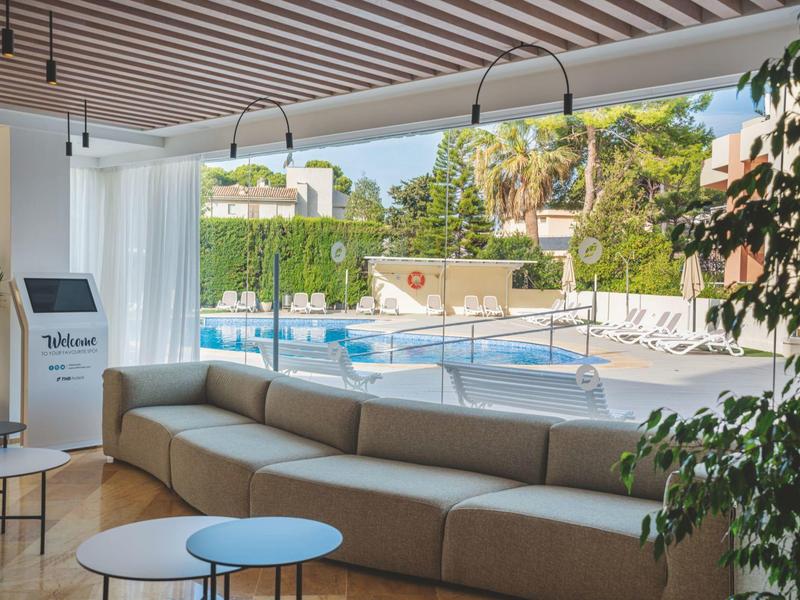 Nowoczesna przestrzeń wypoczynkowa z sofą i widokiem na basen na zewnątrz pod błękitnym niebem.