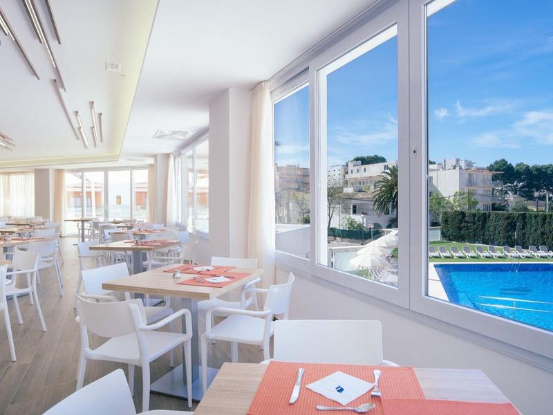 Jasna restauracja z białymi meblami z widokiem na basen i budynki przy czystym niebie.