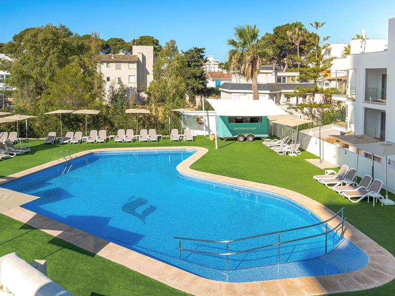 Nowoczesny basen hotelowy z leżakami i zielonym otoczeniem pod błękitnym niebem.