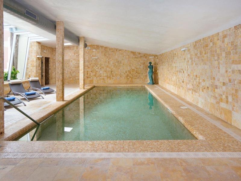 Kryty basen z beżowymi kamiennymi ścianami i niebieskimi leżakami.