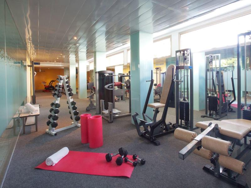 Posilovna s činkami, podložkami a různými posilovacími stroji v světlé místnosti