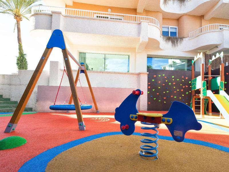 Barevné dětské hřiště s houpačkou a pružinovým houpacím zařízením vedle hotelové budovy.