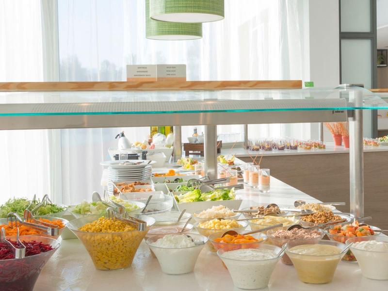 Bufet s různými saláty, omáčkami a přílohami v světlé restauraci.