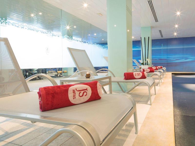 Moderní lehátka s červenými ručníky v světlé lázeňské oblasti s panoramatickými okny.