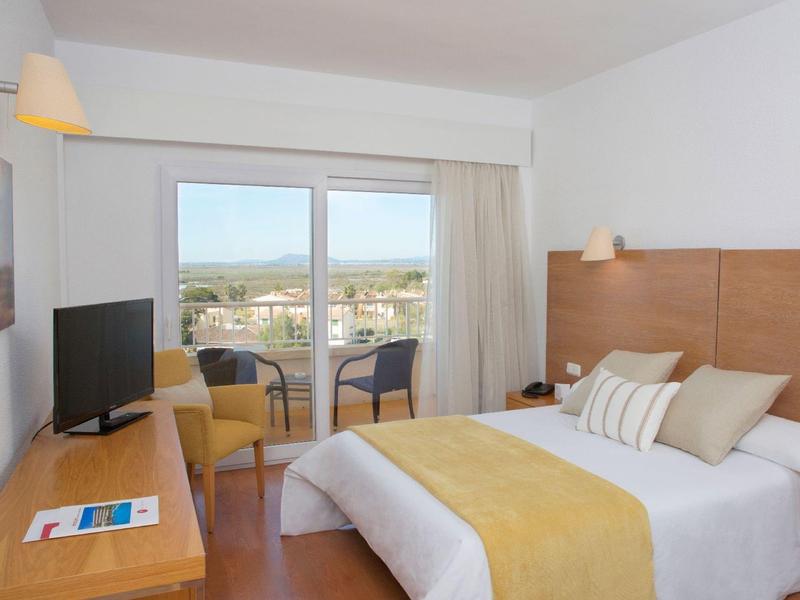 Světý hotelový pokoj s manželskou postelí, televizí a balkonem s výhledem na město.