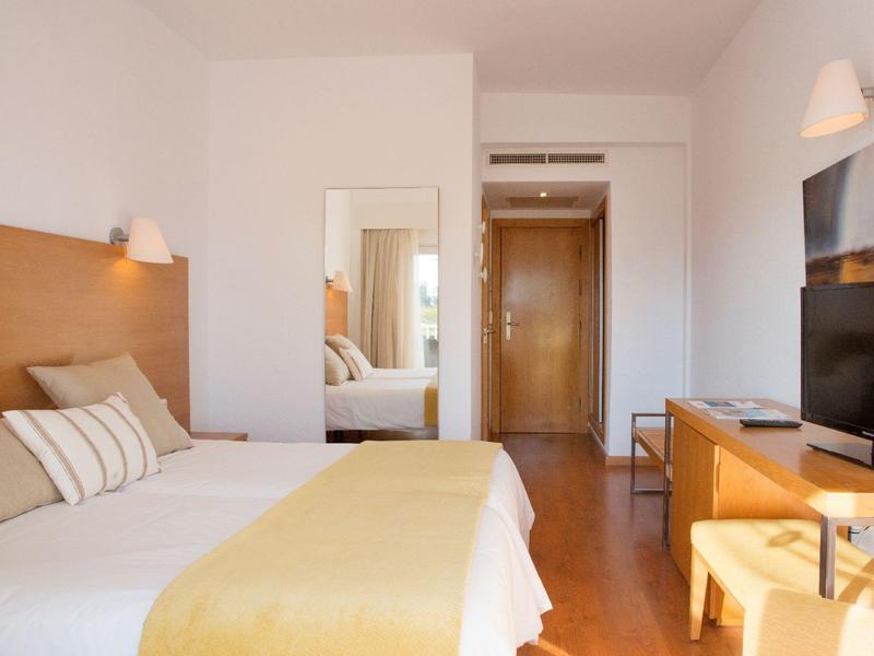 Světý hotelový pokoj se dvěma jednolůžky, žlutými přikrývkami a dřevěným nábytkem.