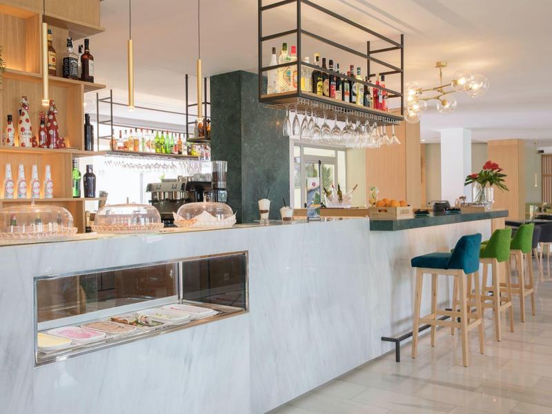 Moderní hotelový bar s světlým pultem, stoličkami a stylovým osvětlením.